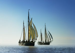 Back light image of two traditional sailing boats under sail, sailing on the ocean. Adventure concept. Reaching for new shores.